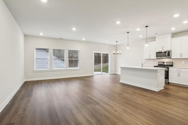 kitchen featuring white cabinetry, decorative light fixtures, stainless steel appliances, dark wood-type flooring, and a kitchen island with sink