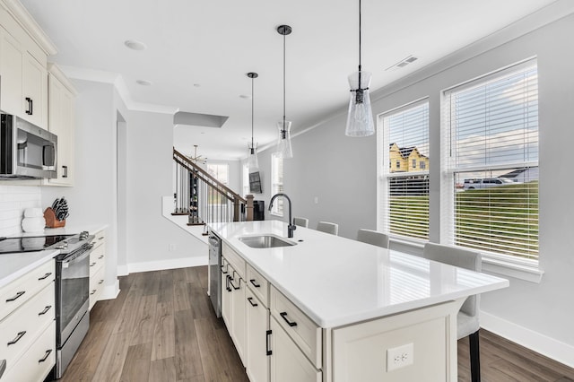 kitchen featuring white cabinetry, hanging light fixtures, an island with sink, appliances with stainless steel finishes, and hardwood / wood-style flooring