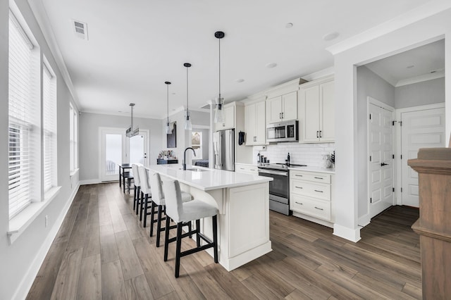 kitchen featuring pendant lighting, white cabinets, a center island with sink, dark hardwood / wood-style flooring, and stainless steel appliances