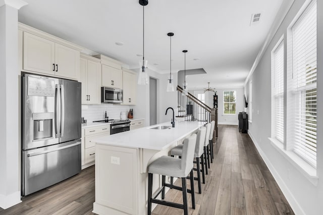 kitchen featuring sink, hardwood / wood-style flooring, an island with sink, appliances with stainless steel finishes, and decorative light fixtures