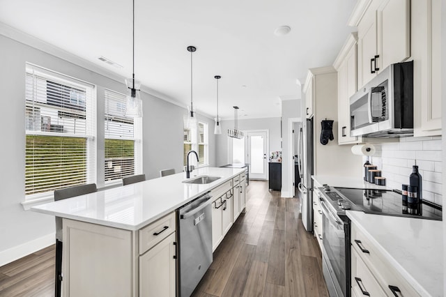 kitchen featuring sink, dark wood-type flooring, decorative light fixtures, a center island with sink, and appliances with stainless steel finishes