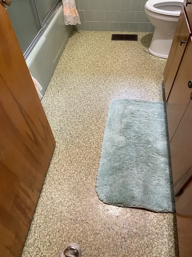 interior details with carpet flooring, toilet, and combined bath / shower with glass door