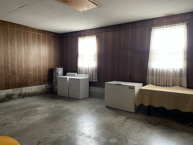 clothes washing area featuring wood walls, water heater, a textured ceiling, and washing machine and clothes dryer