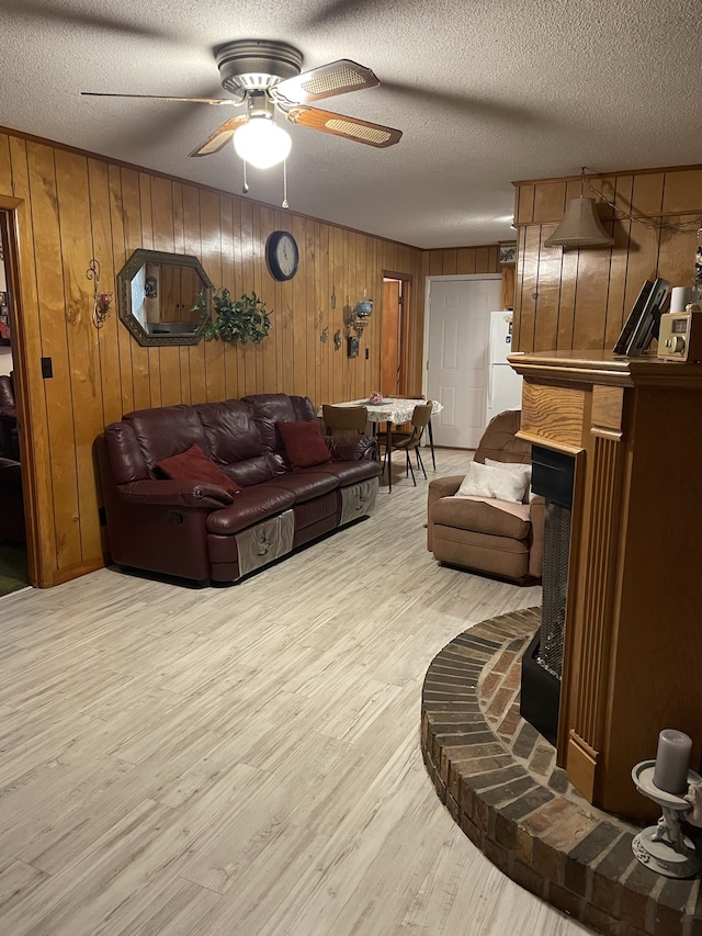 living room with a textured ceiling, light hardwood / wood-style floors, ceiling fan, and wood walls