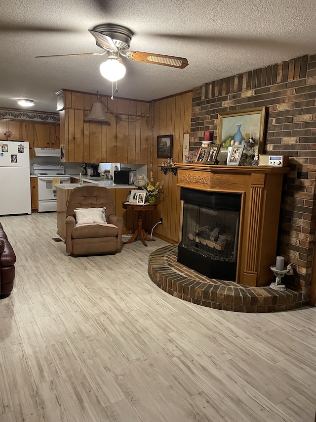 living room with wooden walls, light hardwood / wood-style flooring, ceiling fan, a fireplace, and a textured ceiling