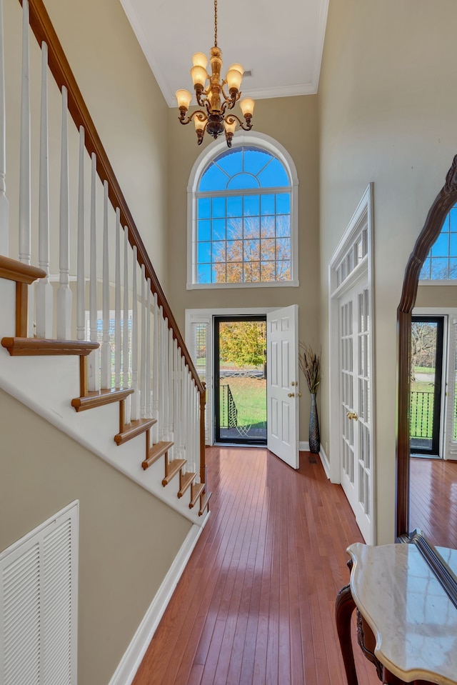 foyer featuring hardwood / wood-style flooring, a towering ceiling, crown molding, and a chandelier