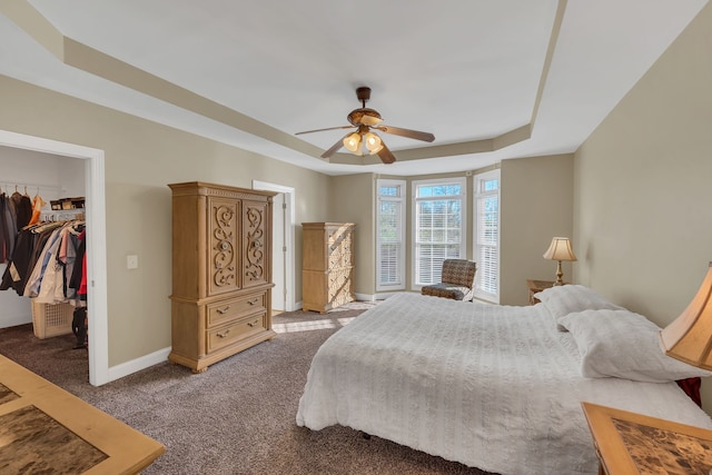 bedroom with a walk in closet, light colored carpet, a raised ceiling, ceiling fan, and a closet