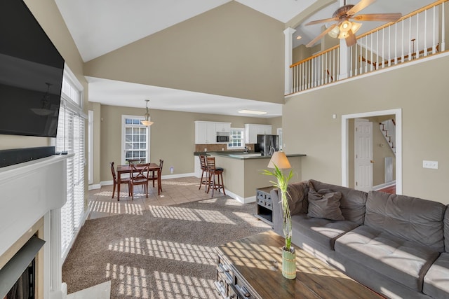 carpeted living room with ceiling fan and high vaulted ceiling