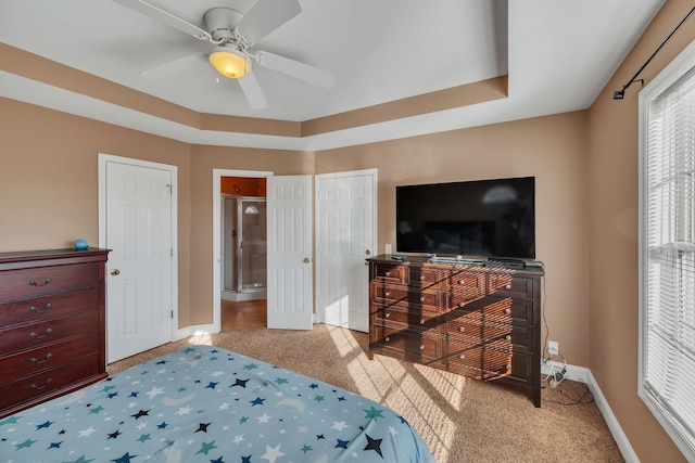 carpeted bedroom featuring a raised ceiling, ceiling fan, and ensuite bathroom