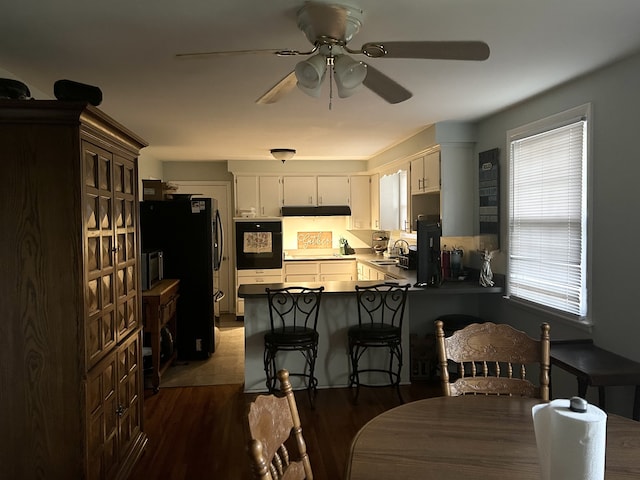 kitchen with black appliances, dark hardwood / wood-style floors, ceiling fan, white cabinetry, and kitchen peninsula