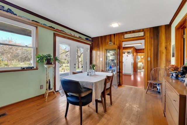 dining space with wooden walls, french doors, light wood-type flooring, and baseboards