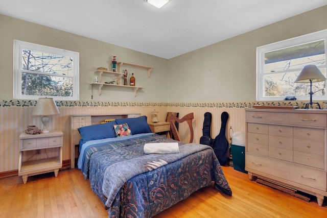 bedroom with multiple windows, light wood-style floors, and wainscoting