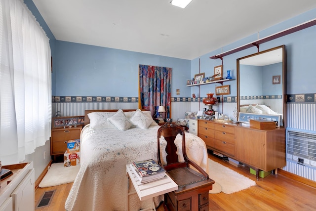 bedroom with visible vents, light wood-style floors, and wainscoting