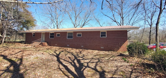 back of house with crawl space, brick siding, and metal roof