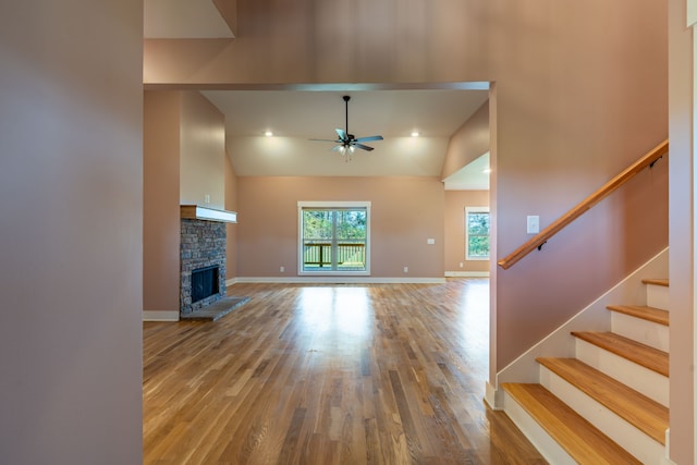 unfurnished living room with hardwood / wood-style flooring, ceiling fan, a stone fireplace, and high vaulted ceiling