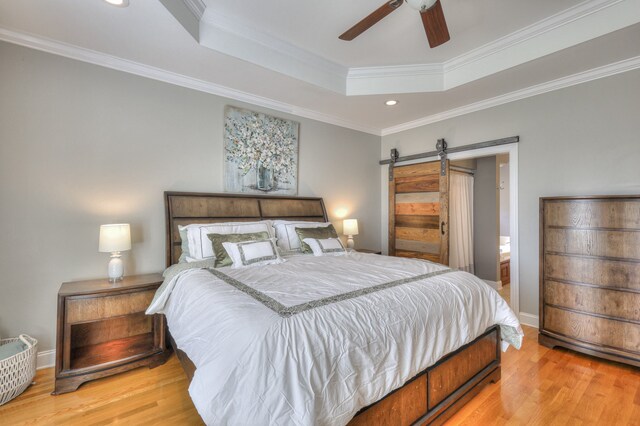 bedroom featuring light wood-type flooring, ensuite bath, ceiling fan, crown molding, and a barn door