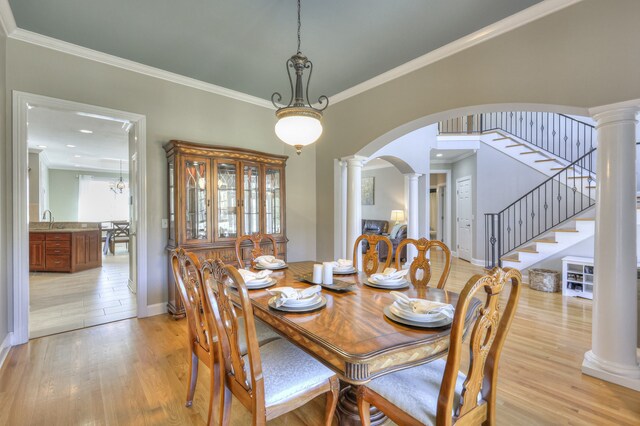 dining area featuring sink, an inviting chandelier, ornamental molding, and light wood-type flooring