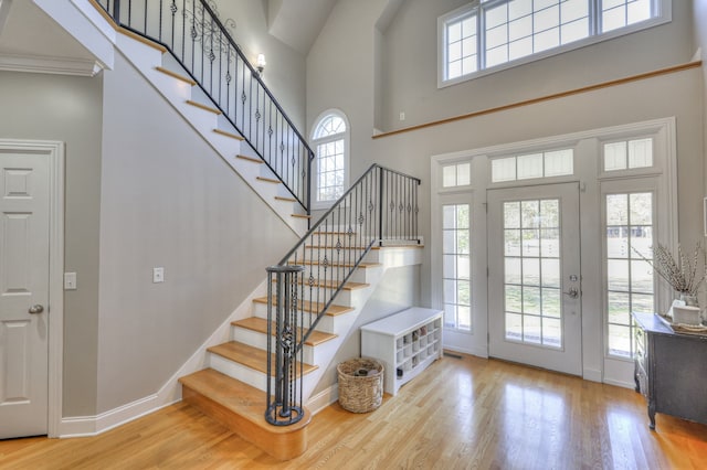 foyer featuring light wood-type flooring, ornamental molding, and a high ceiling