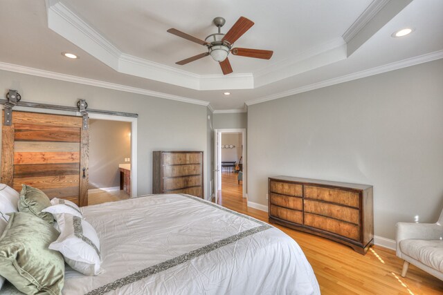 bedroom with ceiling fan, a barn door, crown molding, hardwood / wood-style floors, and a tray ceiling