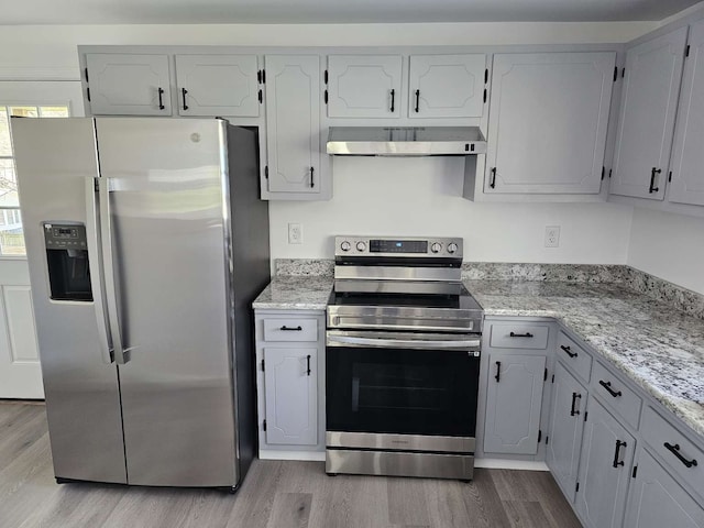 kitchen featuring white cabinets, wall chimney exhaust hood, light wood-type flooring, appliances with stainless steel finishes, and light stone counters