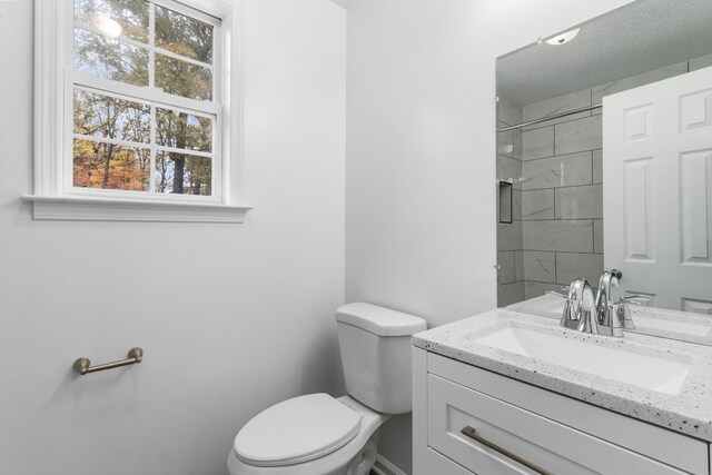 bathroom featuring a tile shower, vanity, and toilet