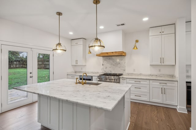 kitchen featuring a kitchen island with sink, white cabinets, sink, high end stainless steel range, and light stone counters