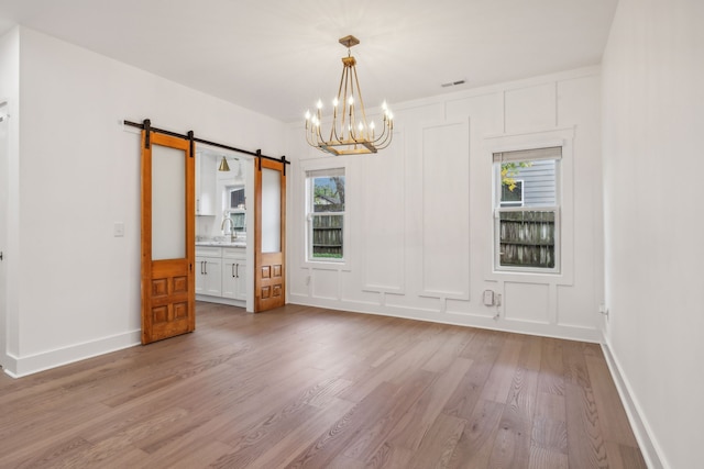 spare room with a chandelier, a barn door, light hardwood / wood-style floors, and plenty of natural light