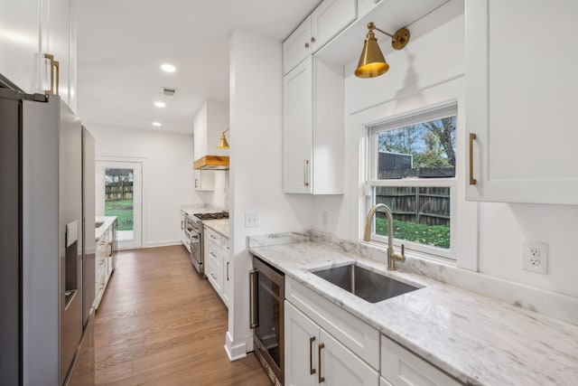 kitchen with sink, light wood-type flooring, white cabinetry, stainless steel appliances, and beverage cooler