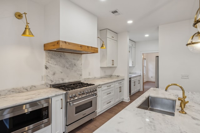 kitchen with light stone countertops, sink, decorative light fixtures, custom range hood, and appliances with stainless steel finishes