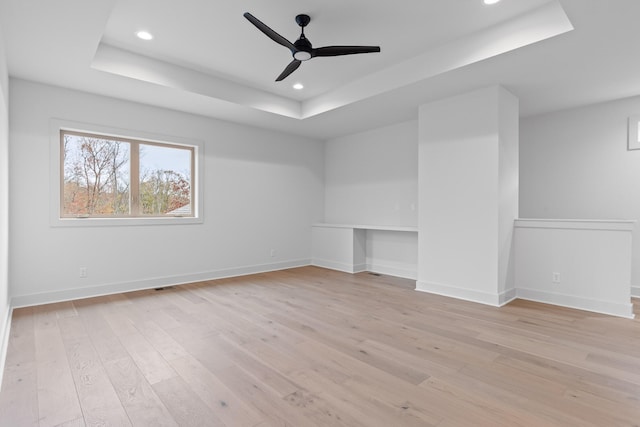 spare room featuring a tray ceiling, ceiling fan, built in desk, and light hardwood / wood-style floors