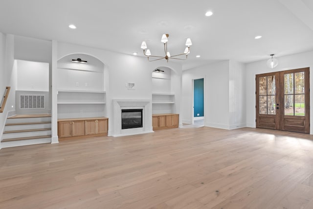 unfurnished living room featuring a chandelier, french doors, built in shelves, and light hardwood / wood-style flooring