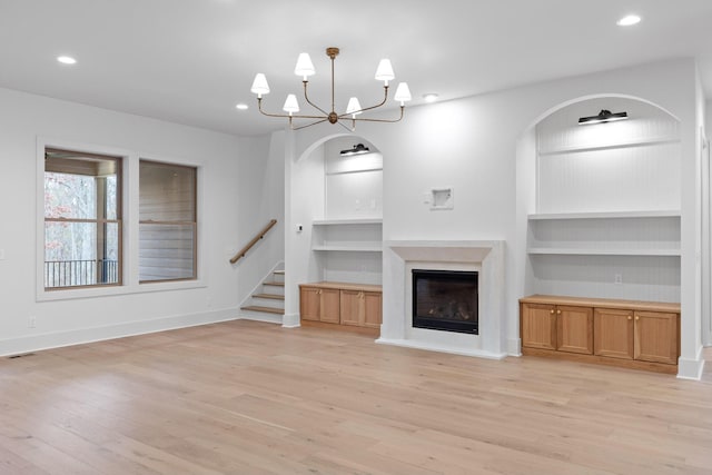 unfurnished living room with built in shelves, light wood-style floors, a glass covered fireplace, a chandelier, and recessed lighting