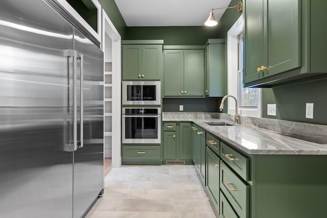 kitchen with built in appliances, green cabinets, light stone countertops, and sink