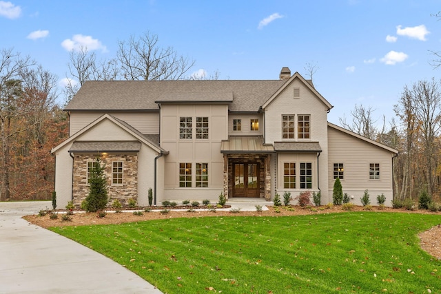 view of front of property with stone siding, roof with shingles, a front lawn, a chimney, and driveway