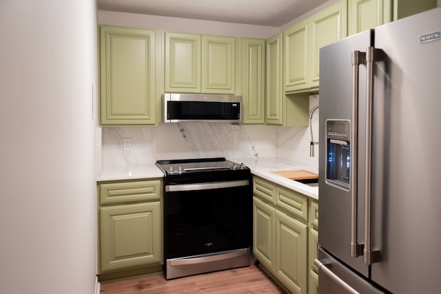 kitchen with green cabinets, light wood-type flooring, a textured ceiling, tasteful backsplash, and stainless steel appliances