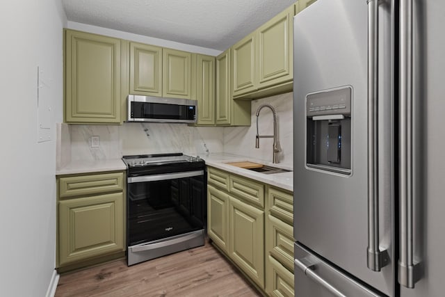 kitchen featuring sink, a textured ceiling, stainless steel appliances, light hardwood / wood-style floors, and decorative backsplash