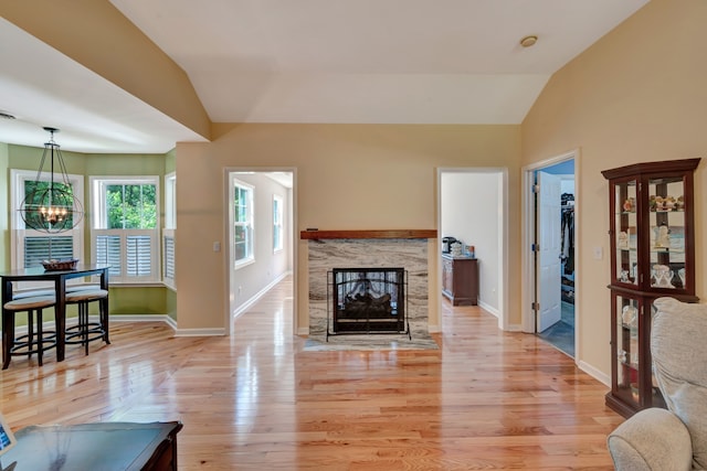 living room with light wood-type flooring, an inviting chandelier, lofted ceiling, and a premium fireplace