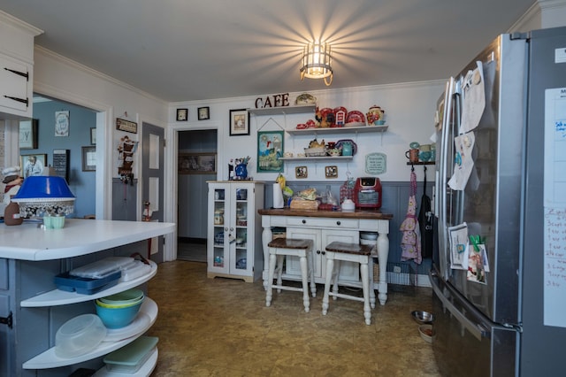 kitchen with white cabinetry, stainless steel fridge, crown molding, and a kitchen breakfast bar