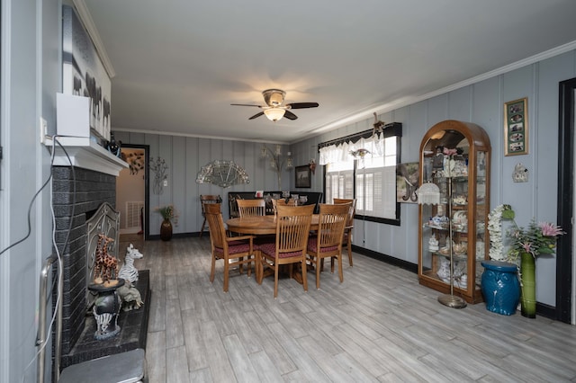 dining area featuring a fireplace, light wood-type flooring, ceiling fan, and ornamental molding