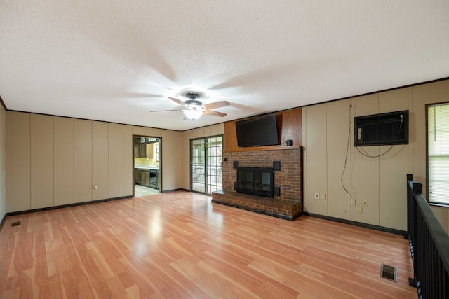 unfurnished living room with light hardwood / wood-style floors, a textured ceiling, a wall mounted AC, and a brick fireplace