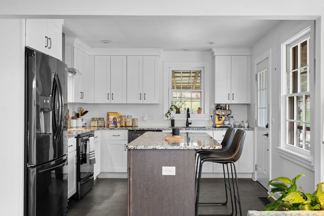 kitchen featuring stainless steel electric range oven, a center island, black refrigerator with ice dispenser, light stone counters, and a kitchen bar