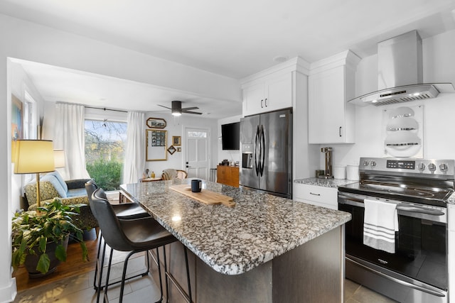 kitchen featuring white cabinetry, wall chimney exhaust hood, stainless steel appliances, a kitchen breakfast bar, and a kitchen island