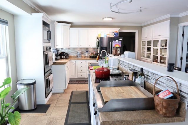 kitchen with decorative backsplash, stainless steel appliances, crown molding, light tile patterned floors, and white cabinetry