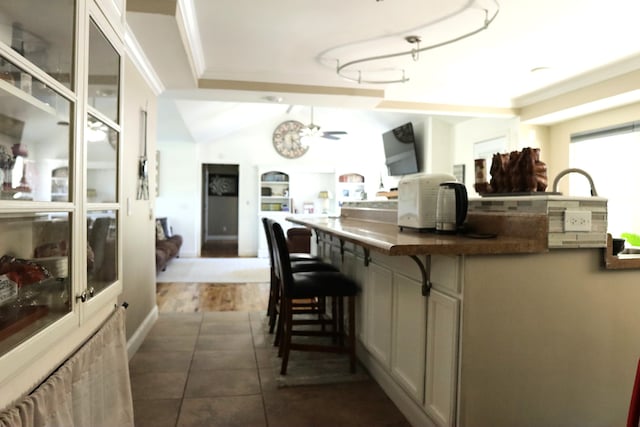 kitchen featuring lofted ceiling, a kitchen breakfast bar, ceiling fan, dark tile patterned floors, and ornamental molding