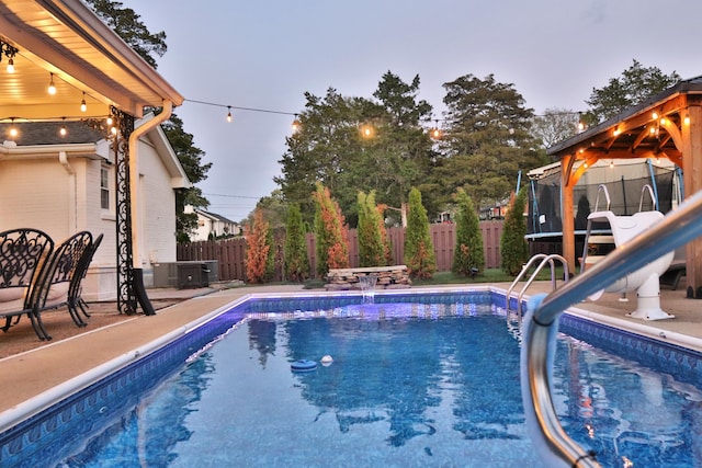 pool at dusk featuring pool water feature and a trampoline