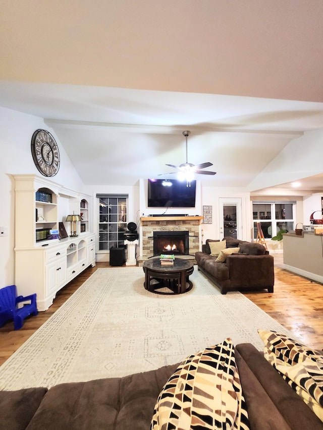 living room with wood-type flooring, a stone fireplace, ceiling fan, and lofted ceiling