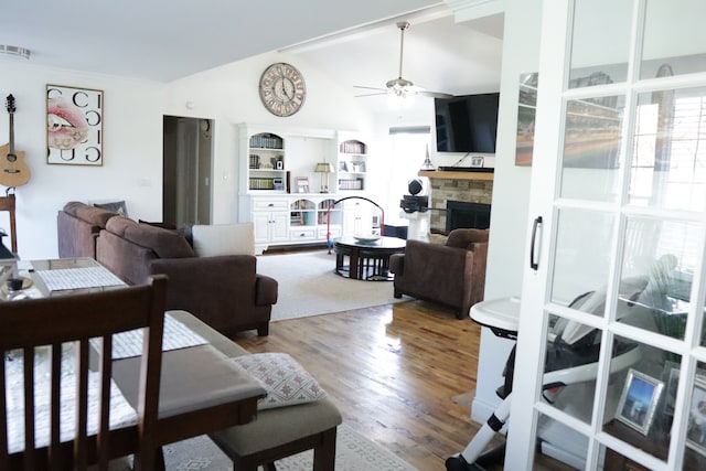 living room featuring built in shelves, ceiling fan, a stone fireplace, lofted ceiling, and hardwood / wood-style flooring