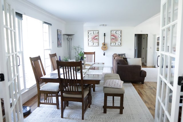 dining room featuring a healthy amount of sunlight, french doors, crown molding, and light hardwood / wood-style flooring