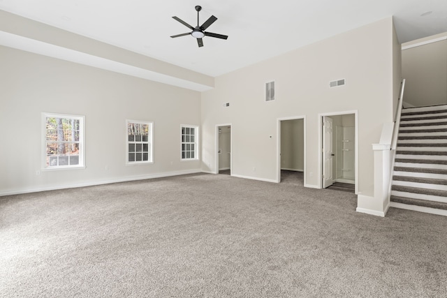 unfurnished living room with ceiling fan, a towering ceiling, and carpet floors