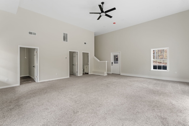 unfurnished living room featuring ceiling fan, light colored carpet, and a high ceiling